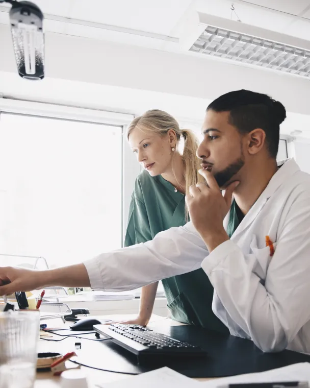 Two colleagues discuss something on a computer screen at a desk